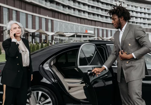 chauffeur opening door of a black limo for the lady on phone